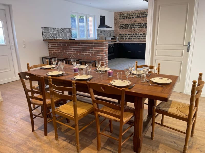 Salle à manger des Gites De Flaubert avec table en bois, couverts dressés et cuisine moderne en brique