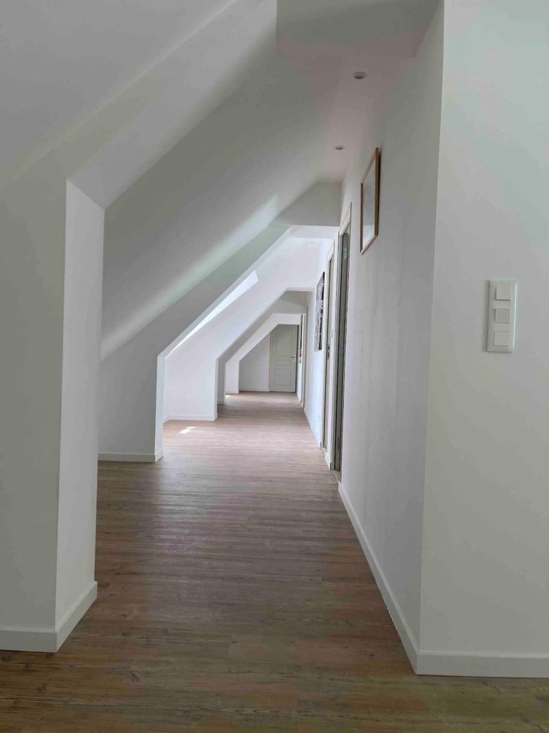 Couloir mansardé lumineux aux murs blancs, plafond incliné et parquet aux Gîtes De Flaubert