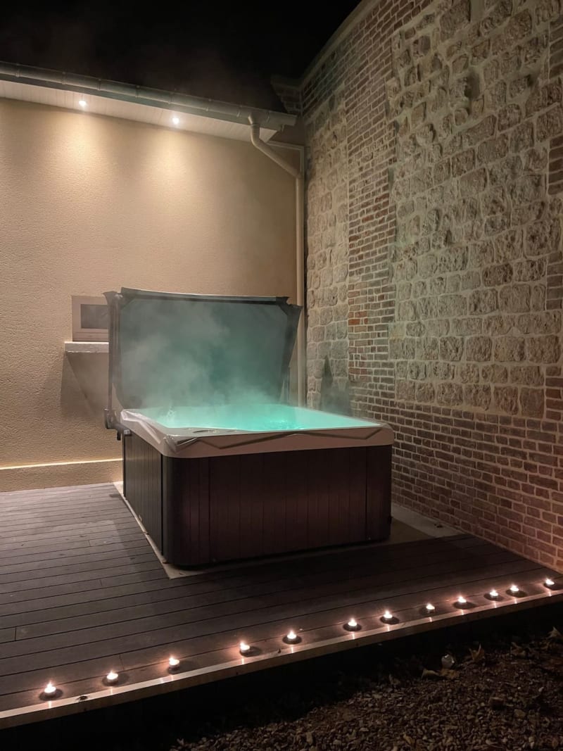 Bain à remous fumant sur terrasse illuminée de la villa Les Gites De Flaubert, mur de briques, ambiance nocturne