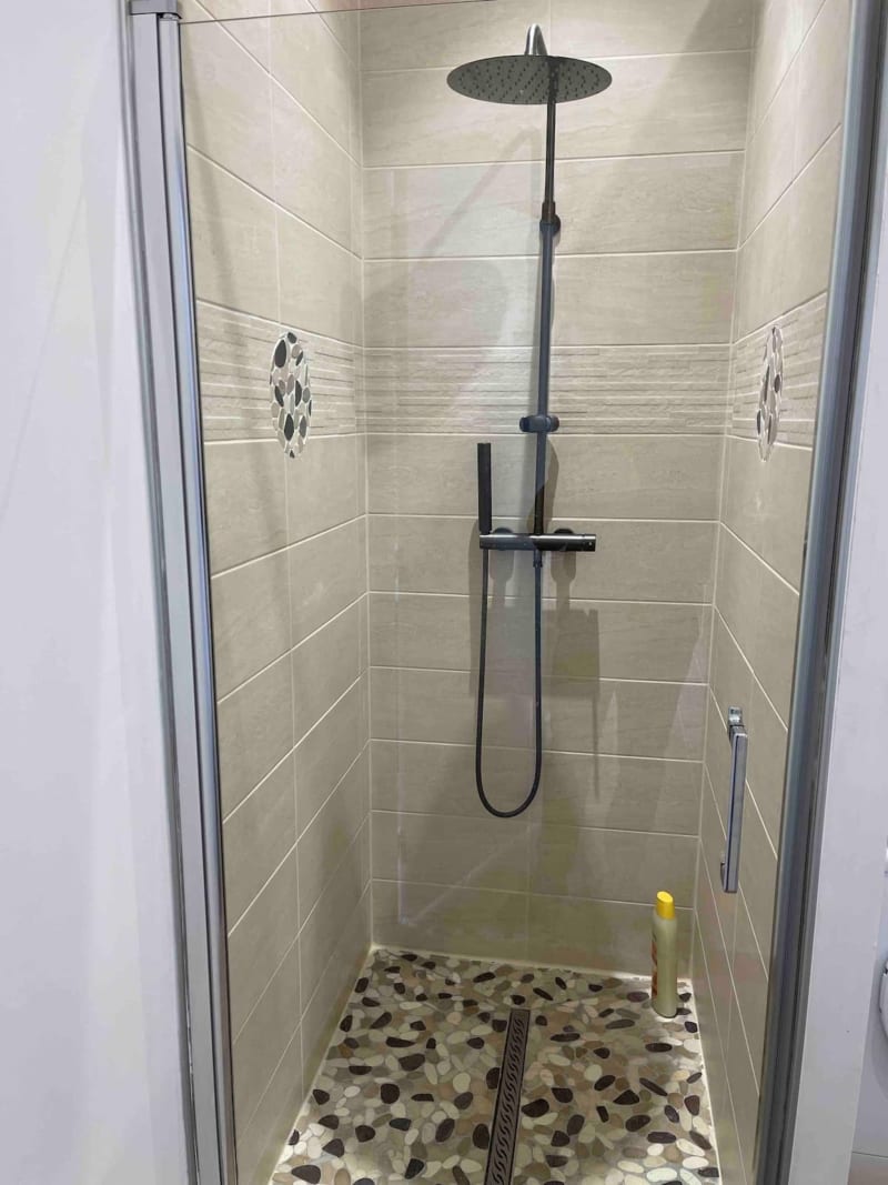 Douche moderne avec robinetterie noire, sol en galets de pierre et carrelage horizontal aux Gîtes De Flaubert