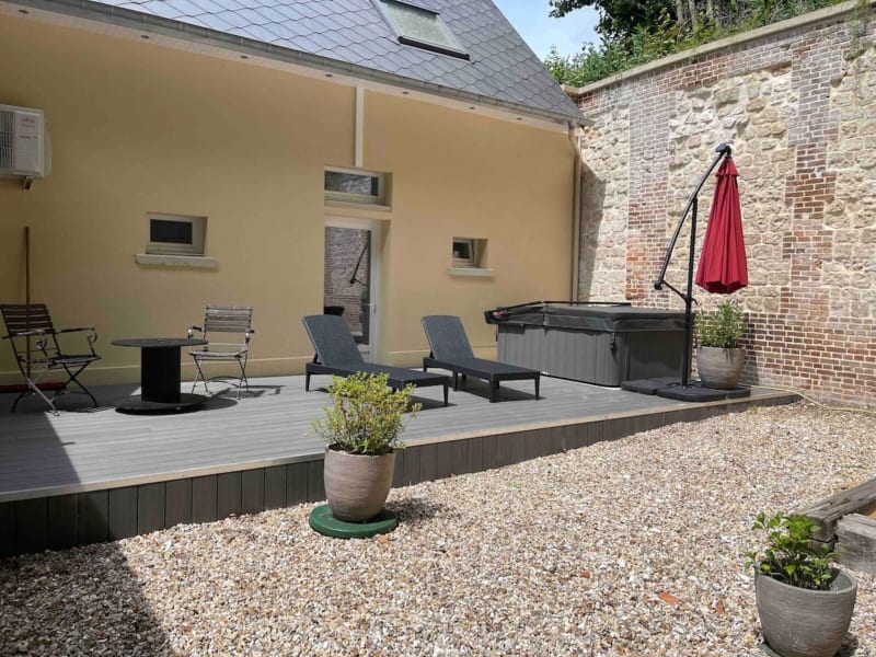 Terrasse moderne aux Gites De Flaubert avec chaises longues, foyer, parasol rouge et mur en brique