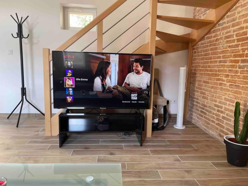 Salon moderne avec Netflix sur TV, poutres en bois et mur de brique aux Gîtes de Flaubert au Héron, France