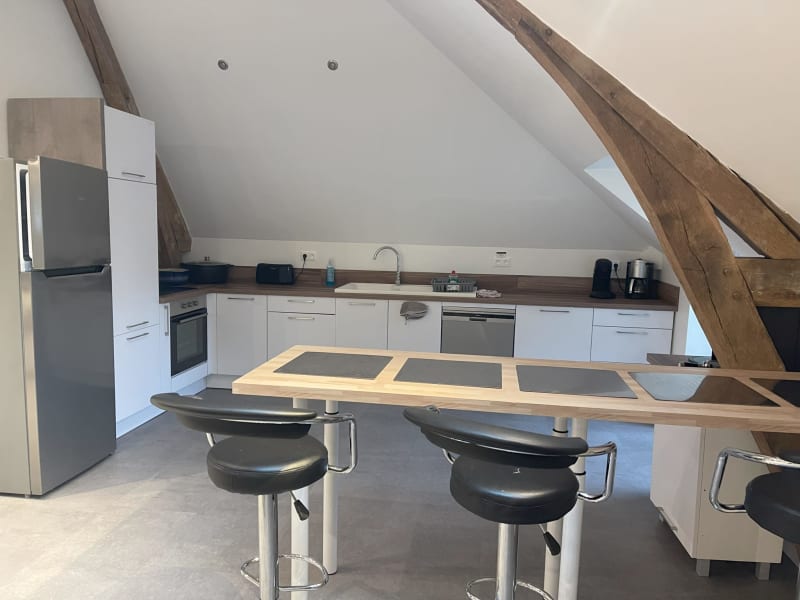Cuisine moderne mansardée aux Gîtes De Flaubert : armoires blanches, poutres bois, îlot avec coin repas et inox
