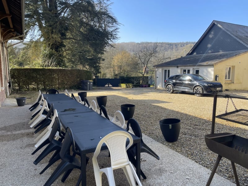 Terrasse de restaurant en plein air aux Gîtes De Flaubert avec table noire, chaises blanches et vues sur la campagne française rurale