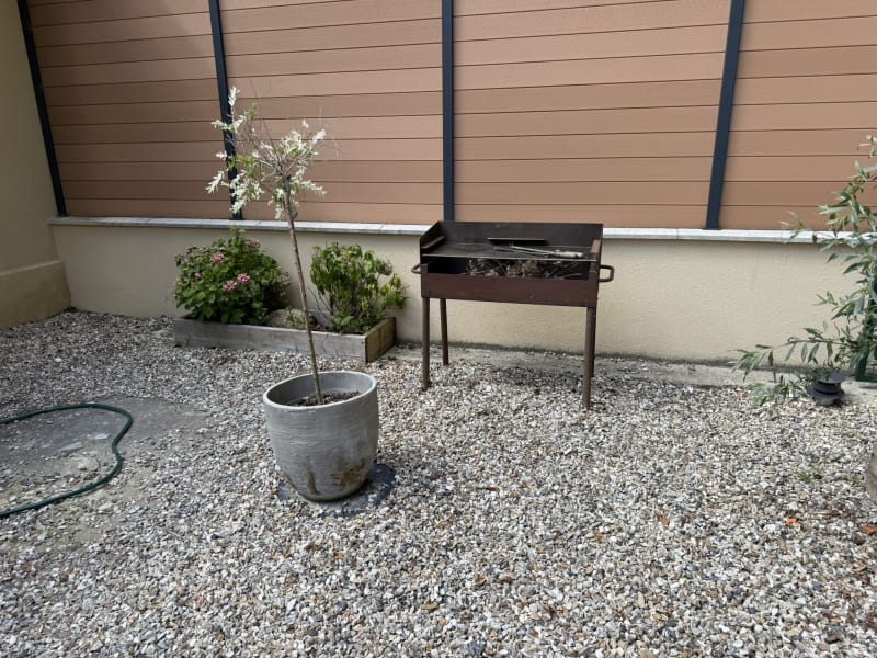 Terrasse extérieure de la villa Les Gites De Flaubert avec sol en gravier, plantes en pots, barbecue et jardin clôturé