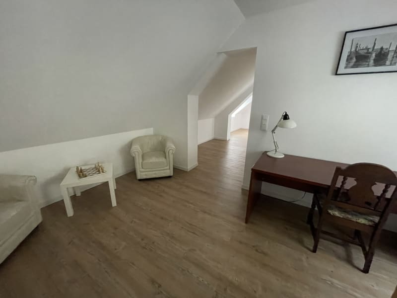 Spacieux salon mansardé à la villa Les Gites De Flaubert avec fauteuil crème, bureau, parquet et escalier