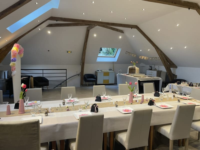 Élégante salle à manger de la villa Les Gites De Flaubert avec table longue, chaises beige, compositions florales roses et poutres apparentes