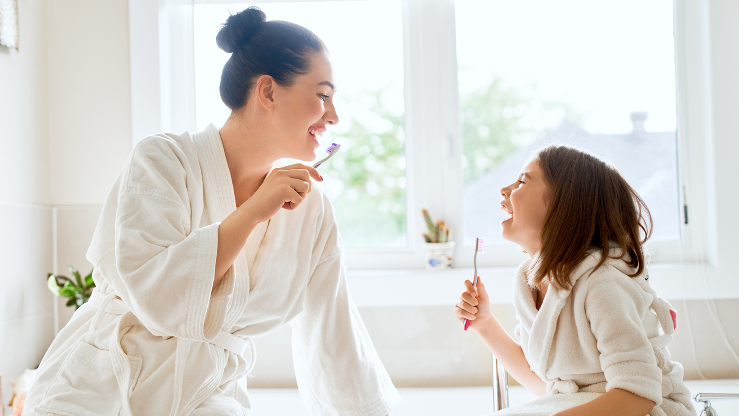 A lady and a child brushing their teeth in the bathroom.