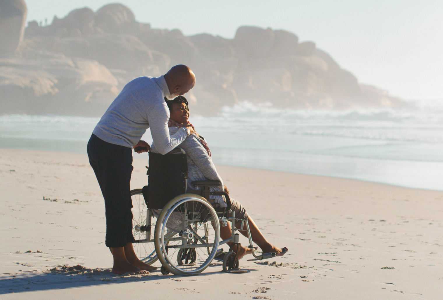 Image of a couple at the beach with wife in a wheel chair sharing a good time.