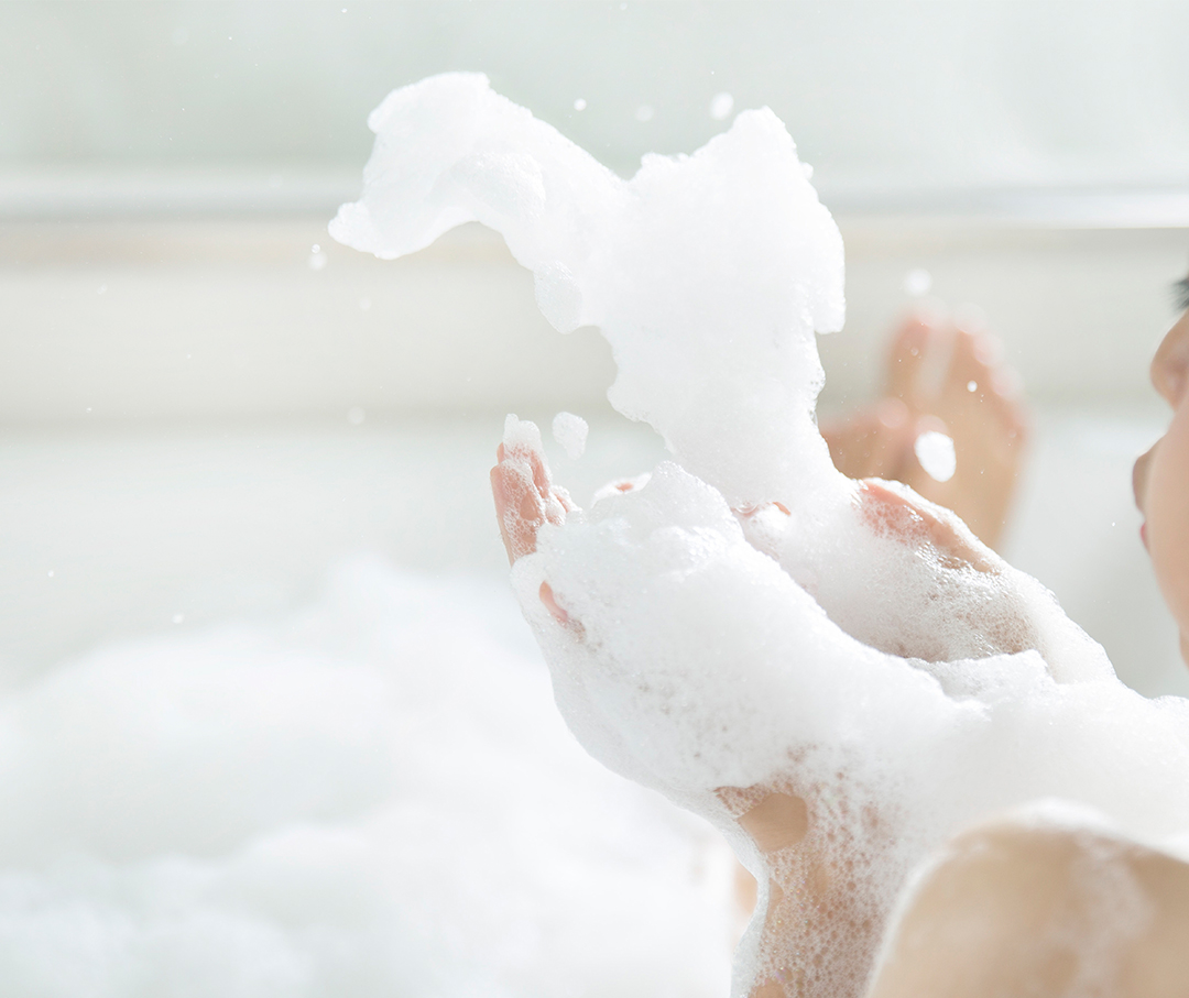 Image of female in soaking tub blowing suds out of hands