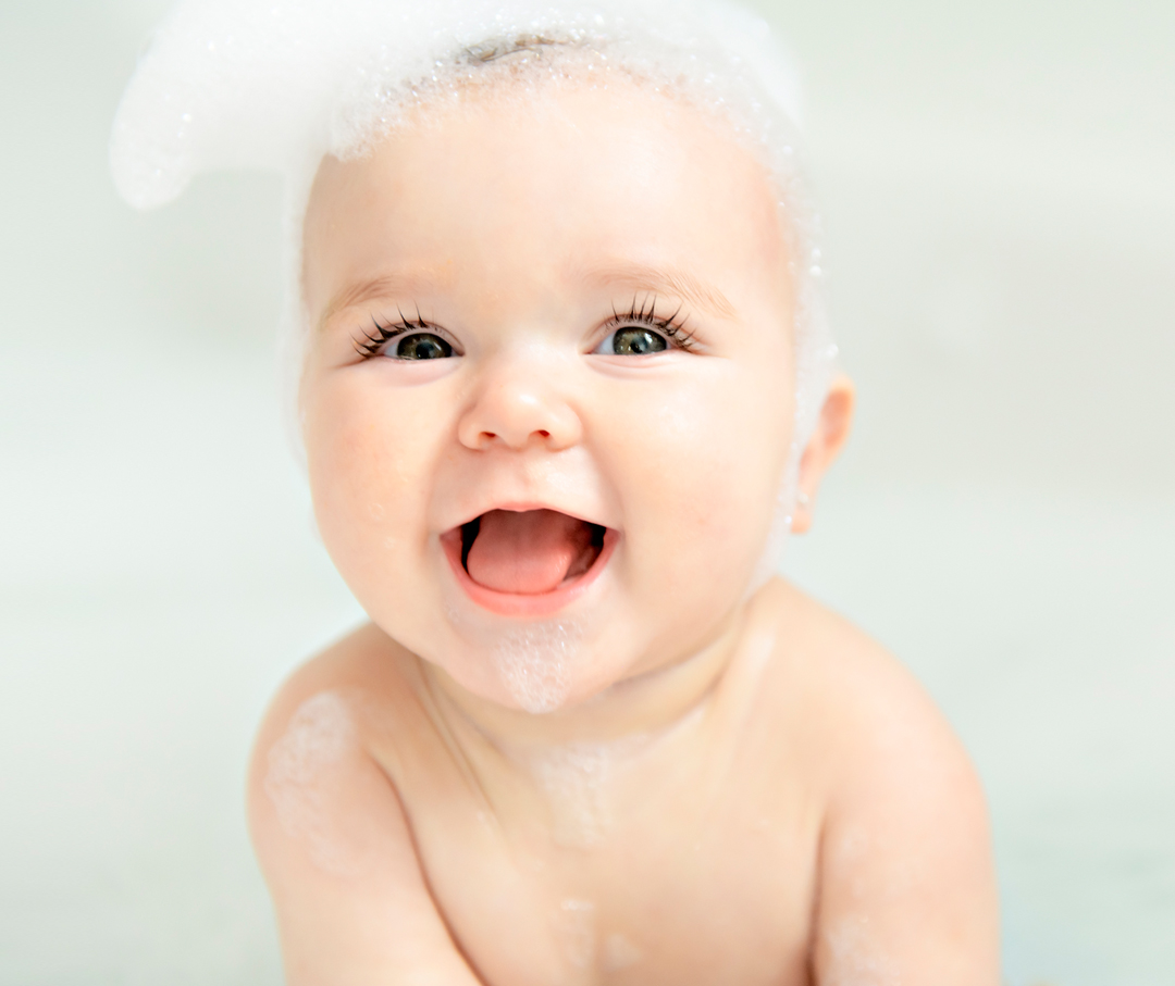 Image of baby with soap suds on head looking into camera and smiling