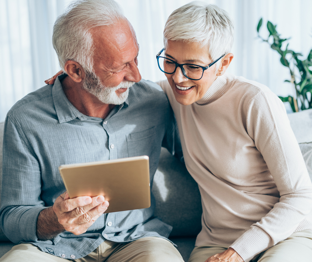 An old couple is happily looking at a tablet.