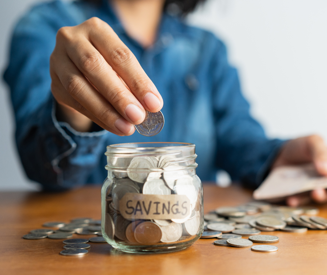 Image of someone placing money into a savings jar.