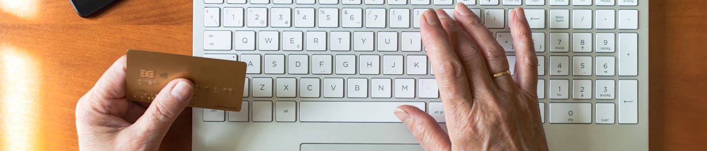 A pair of older hands with one hand holding a credit card and the other hovering over a keypad.