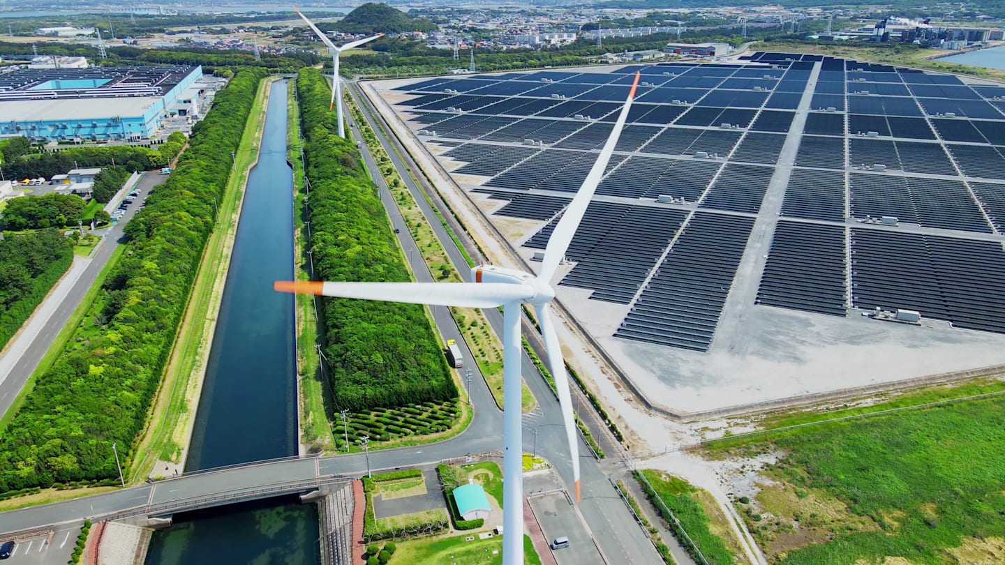 Wind turbines next to solar panels in urban setting.