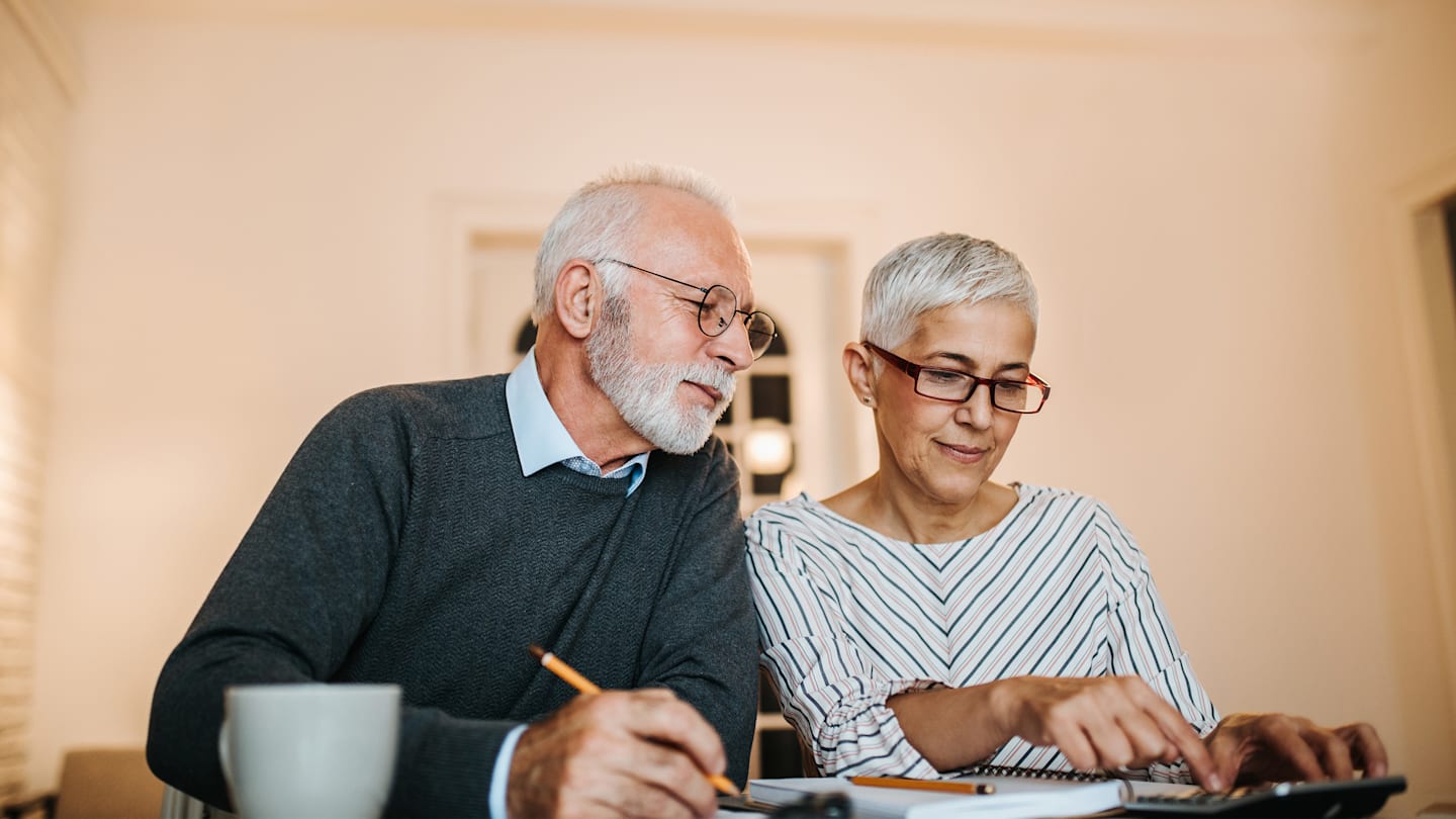 Retiree couple with pencils and notebooks, calculating their post-retirement tax strategy.