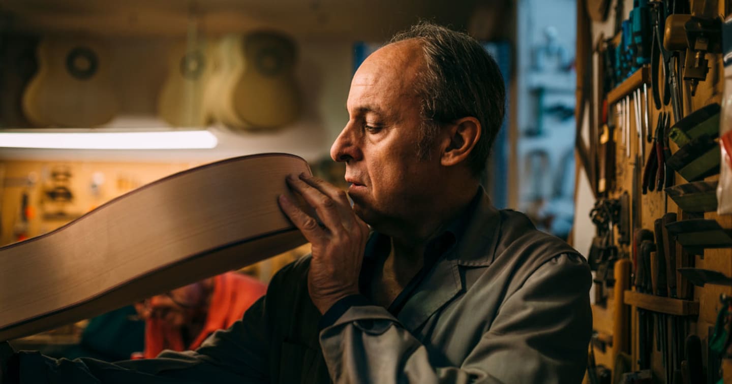 An older man looking at the wood pieces he is using to make a guitar.