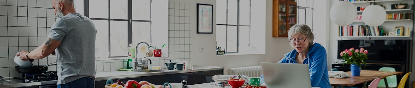 Man in kitchen cooking with woman sitting at the counter working on a laptop