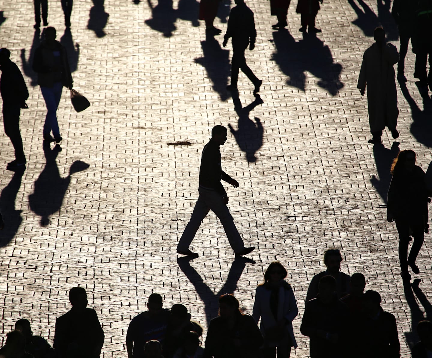 Shadowed figures walking on city street.