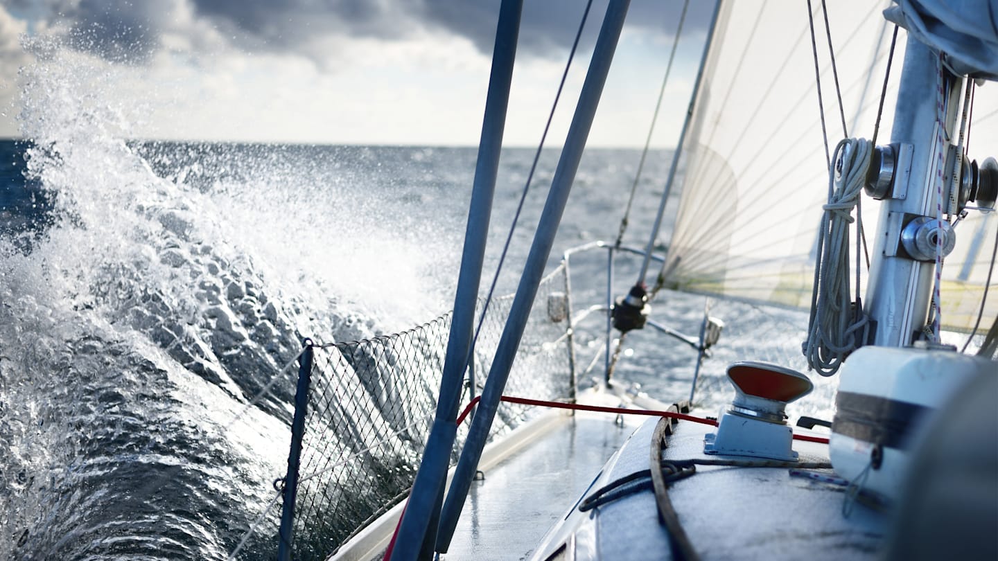 Waves crashing on sailboat in water.