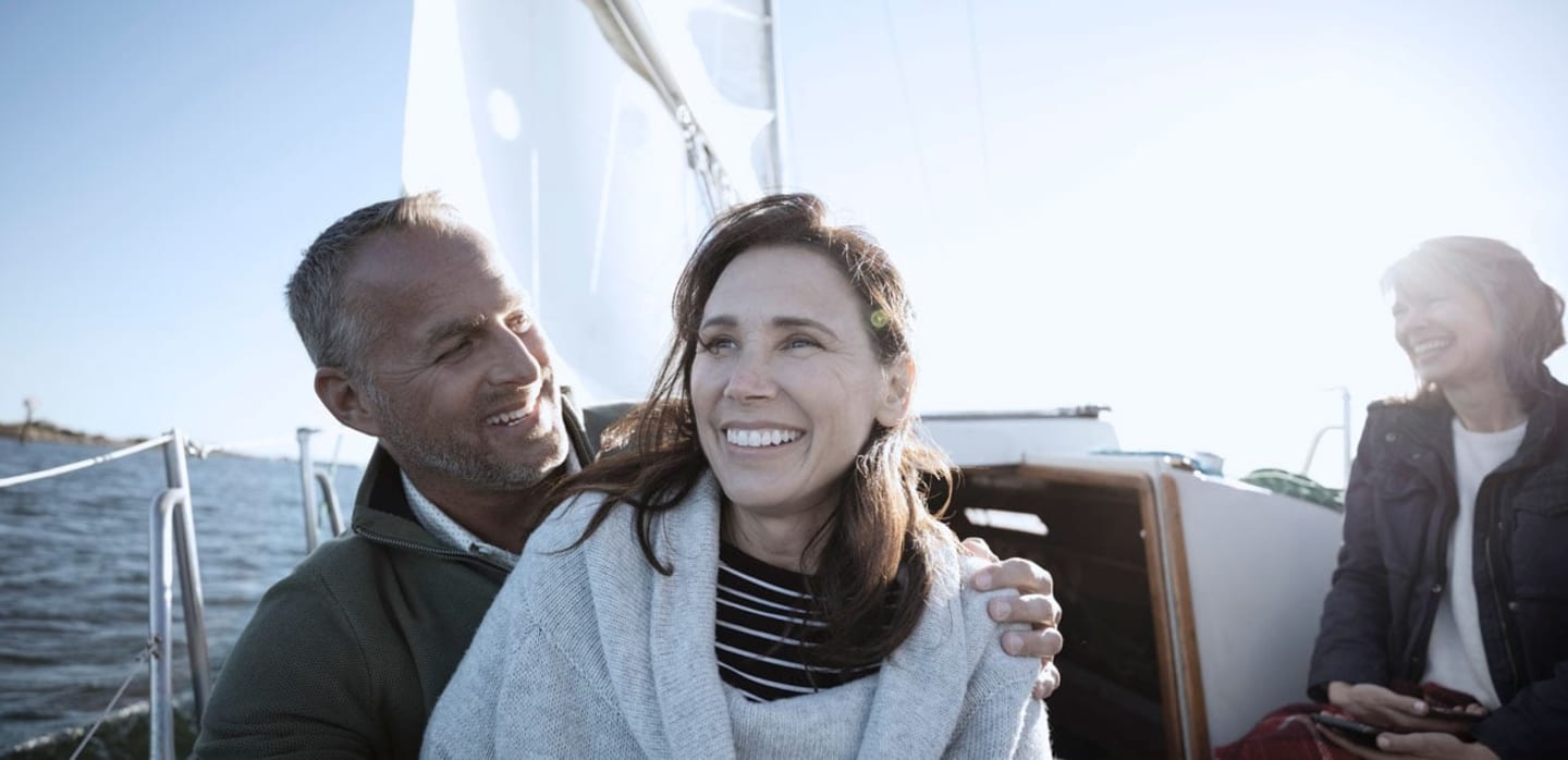 Couple enjoying a sailboat ride with the sun behind them.