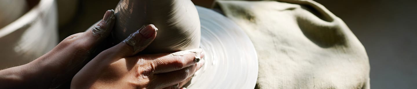 A close-up image of hands shaping clay on a potter's wheel.