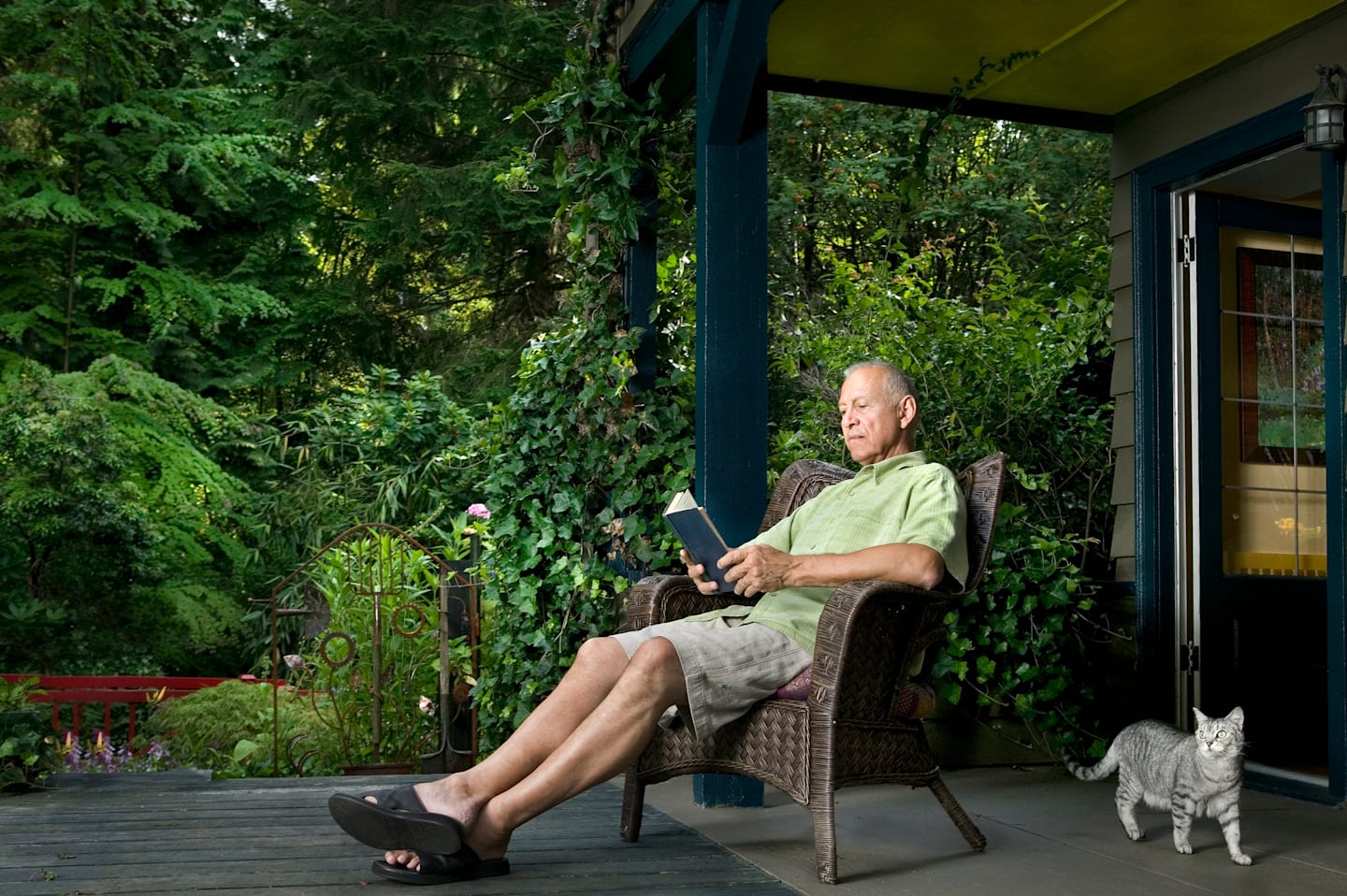 Older man sitting on front porch of house in summer time.