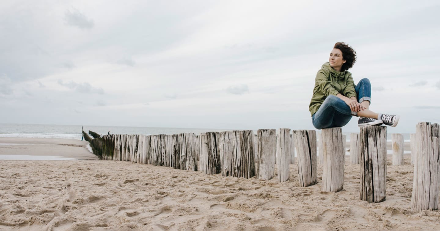 A woman sitting on logs on the beach.