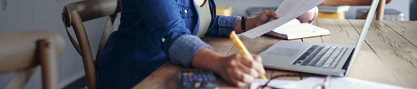 A woman sitting at her desk surrounded by papers, a laptop and a calculator.