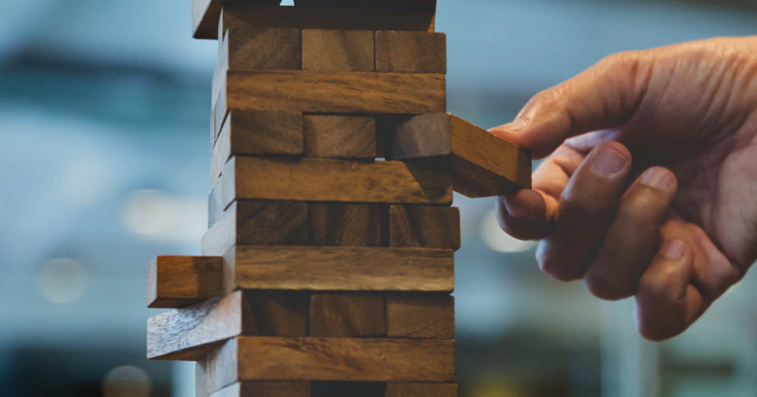 Hand pulling wood piece from tumbling tower game.
