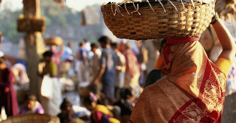 Woman holding basket on head in crowd with others.