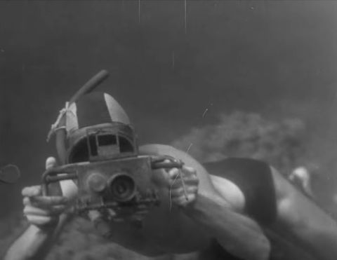 An early underwater camera housing. From the film “Becoming Cousteau.” Note that the upside-down orientation of the camera, the wrench-like lever (meant to control film advance), and the cumbersome and inaccurate sports viewfinder.