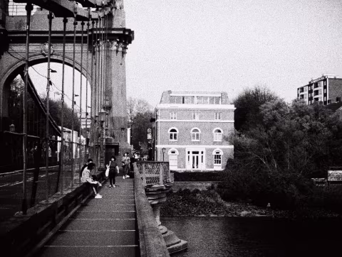 There are pedestrian walkways on both sides of the central carriageway. The wooden plank flooring is visible. This view is from the Barnes side walking towards the Hammersmith side of the Thames.
