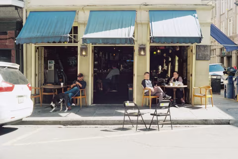 A cafe that opens up to the street with three French doors and a few patrons dining in front.