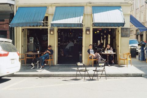 A cafe that opens up to the street with three French doors and a few patrons dining in front.