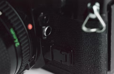 The DOF preview lever (the black buckle to the side of the lens) can be locked into place for stop-down metering and unlocked by pressing the silver button that’s visible underneath the lever once it’s pushed in. Above the lever is an exposure lock button (with a silver ring around it) and an Exposure Memory Switch.