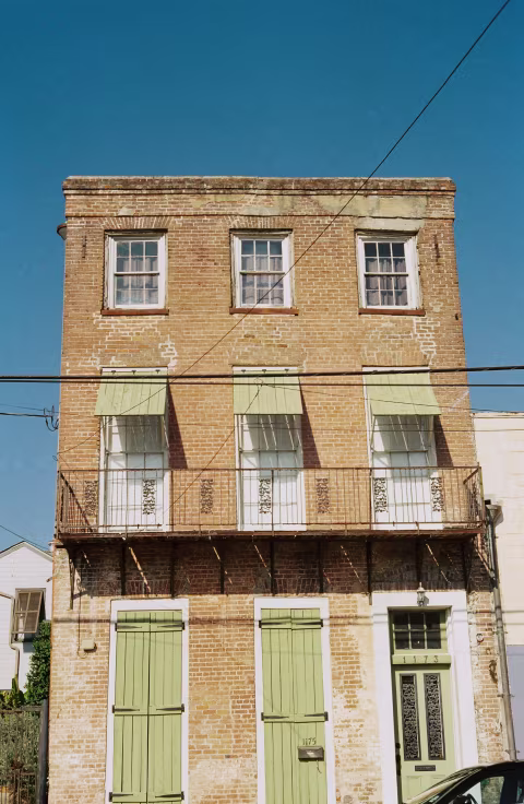 A three-story brick building with green doors and awnings, less furnishings with each floor moving up.