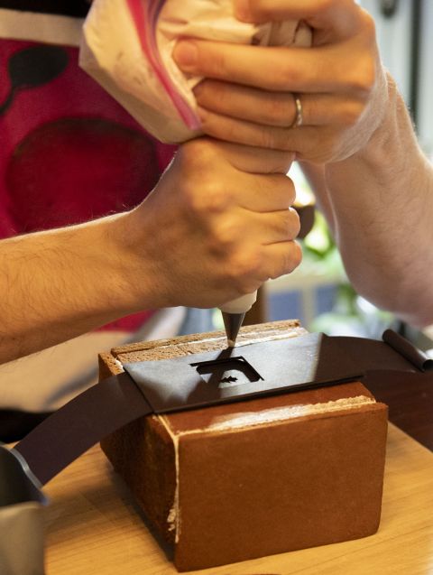 The assembly begins. The paper shutter/aperture components are placed carefully on top of the gingerbread camera’s front piece of bread directly over the lens opening.