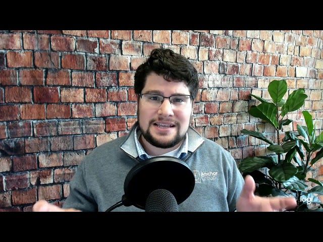 A man wearing glasses speaks into a microphone, engaged in a conversation or presentation.