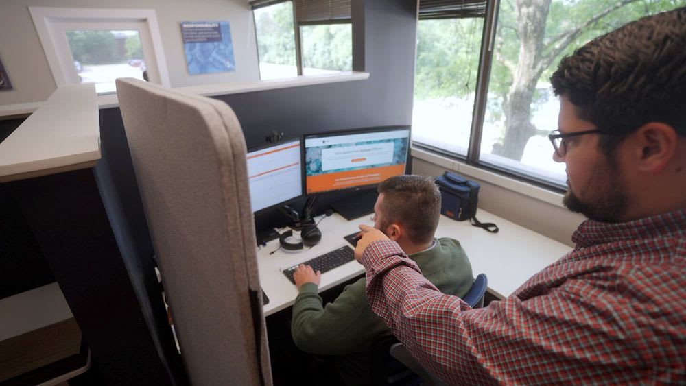 Two men collaborate on a computer, focused on the screen and engaged in a learning activity together.
