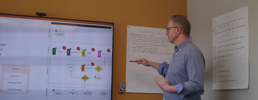 anchor group employee standing and presenting, explaining a graph on a screen