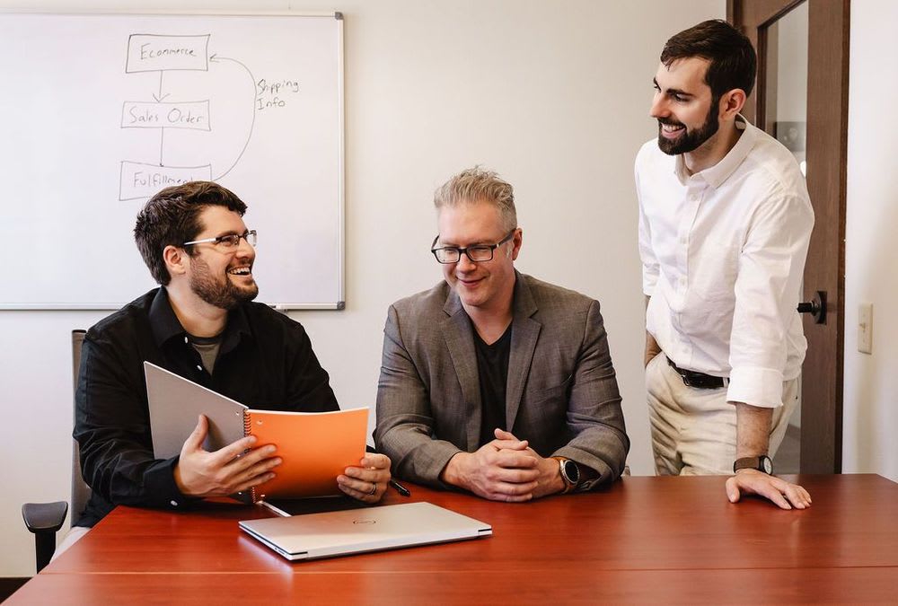 Three people engaged in collaboration over a document held open between them.