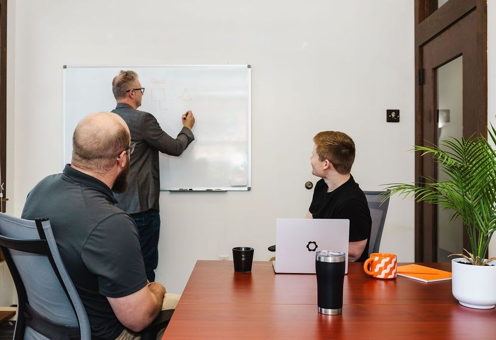A person working on a whiteboard while two people watch attentively.