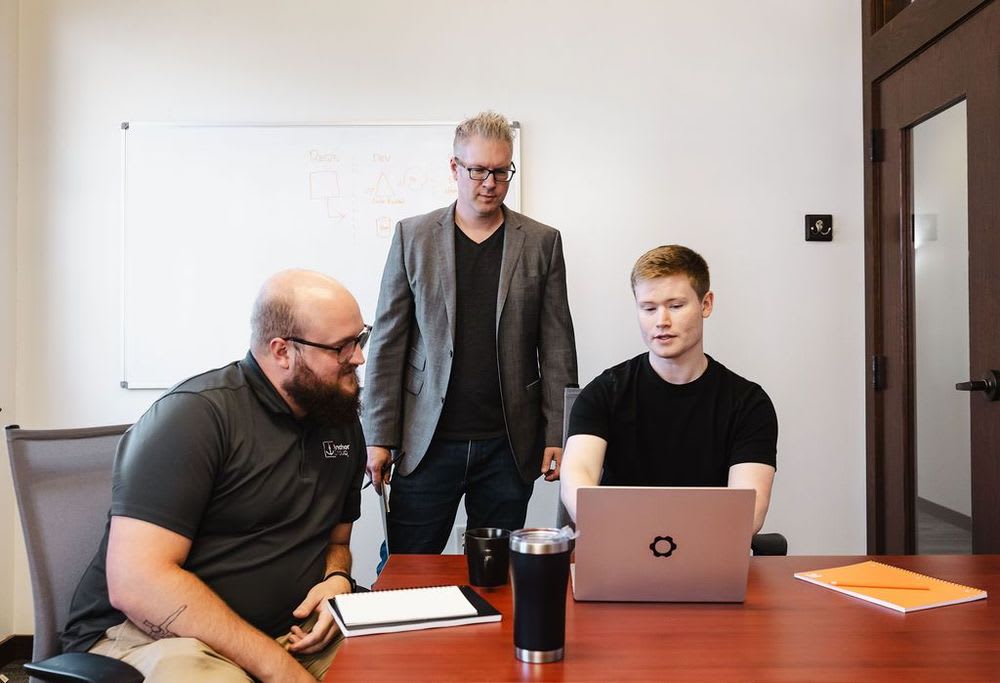 Three people closely collaborating over a laptop.