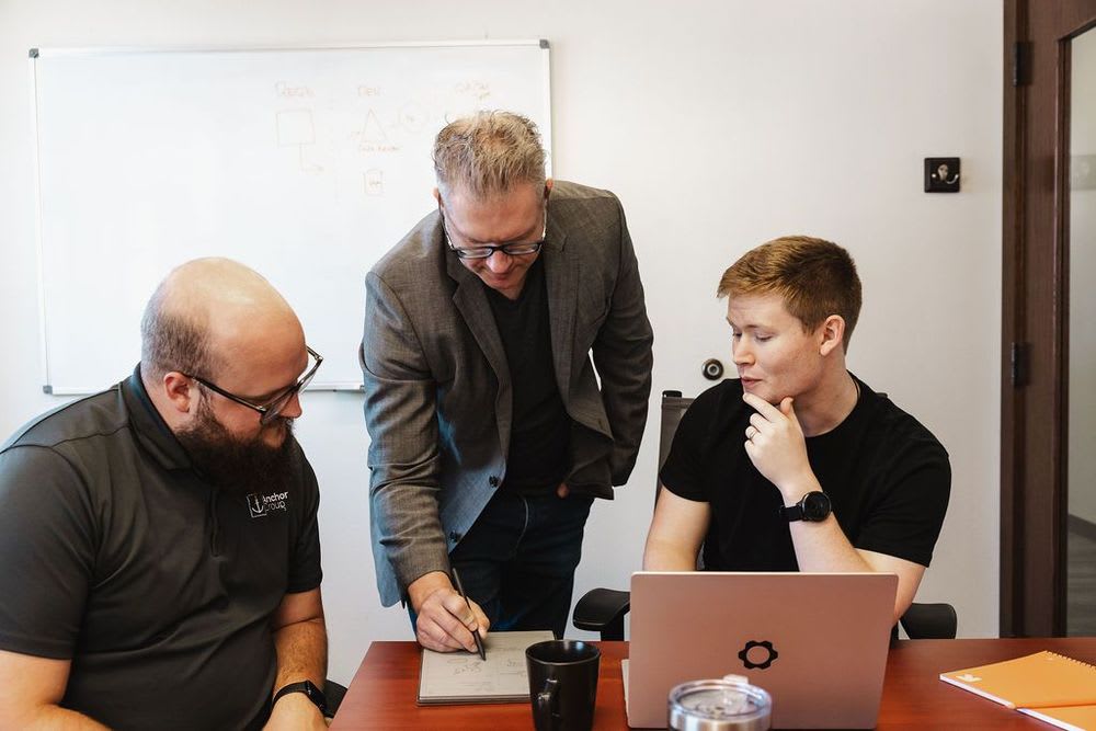 Three people collaborating openly over an iPad, laptop, and notebook.