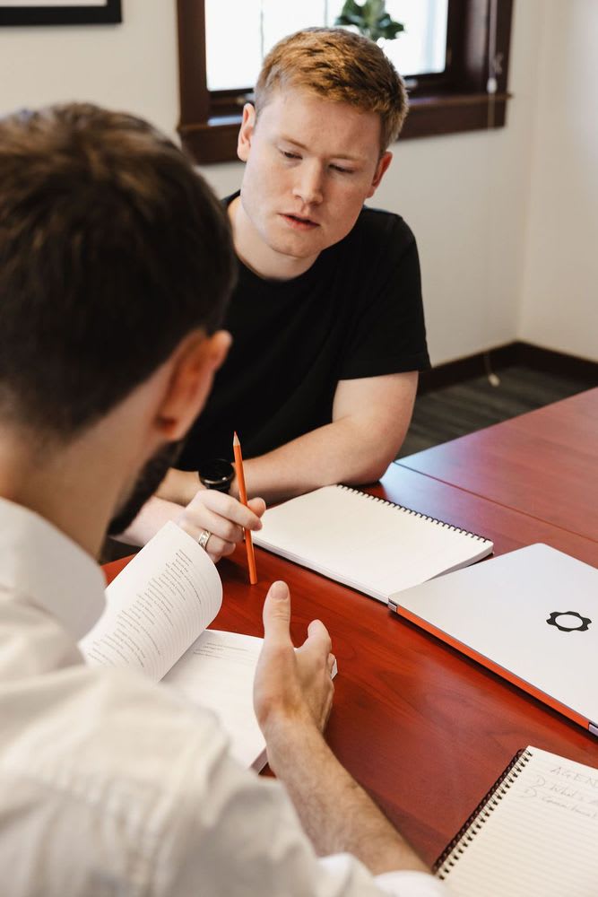 Two men discussing over notebooks and laptops.