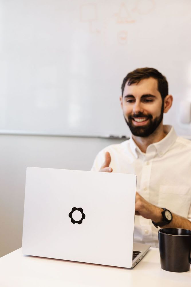 A man smiling contentedly at his laptop with a coffee cup beside him.