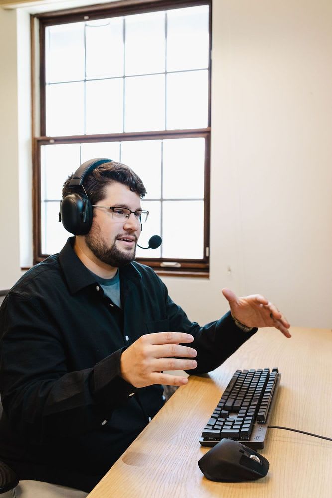 A man in a black shirt speaking emphatically over a keyboard.