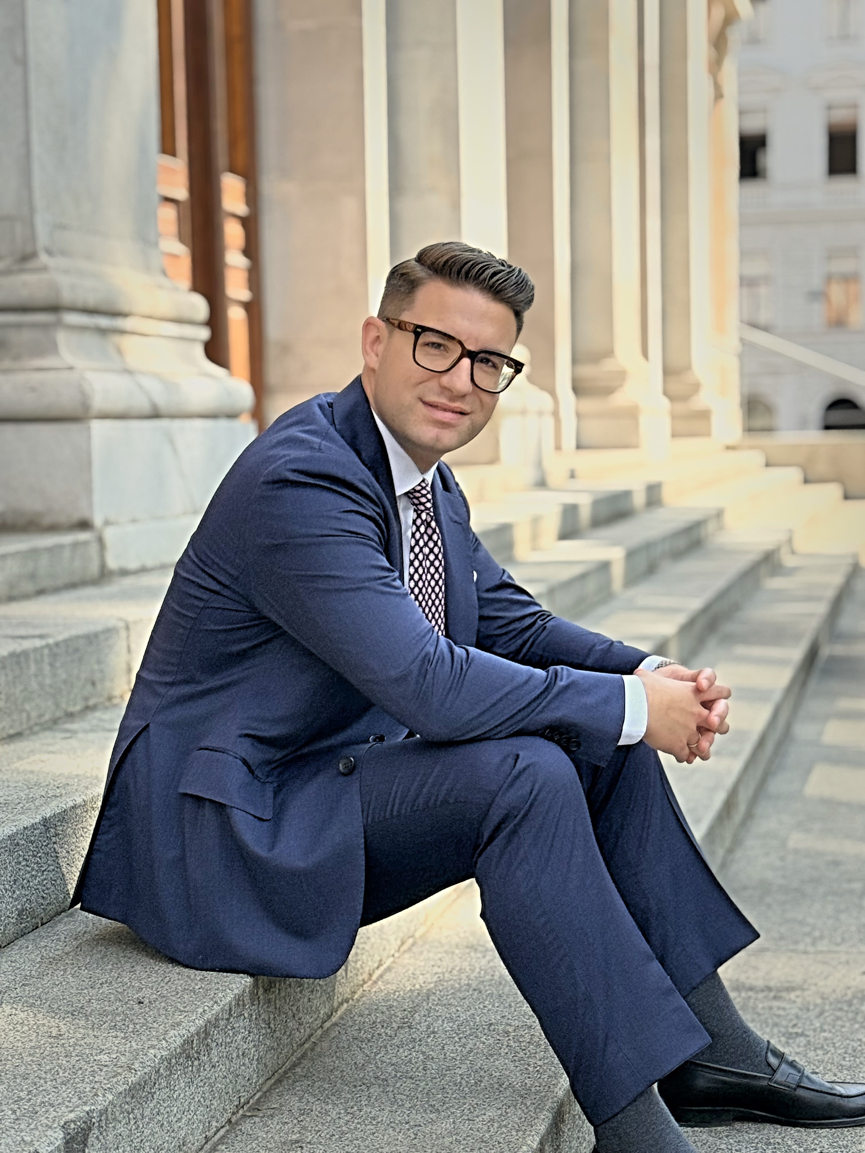 Porträt von Mag. Adrien Bompard, LL.M., auf den Stufen eines klassizistischen Gebäudes in Wien
