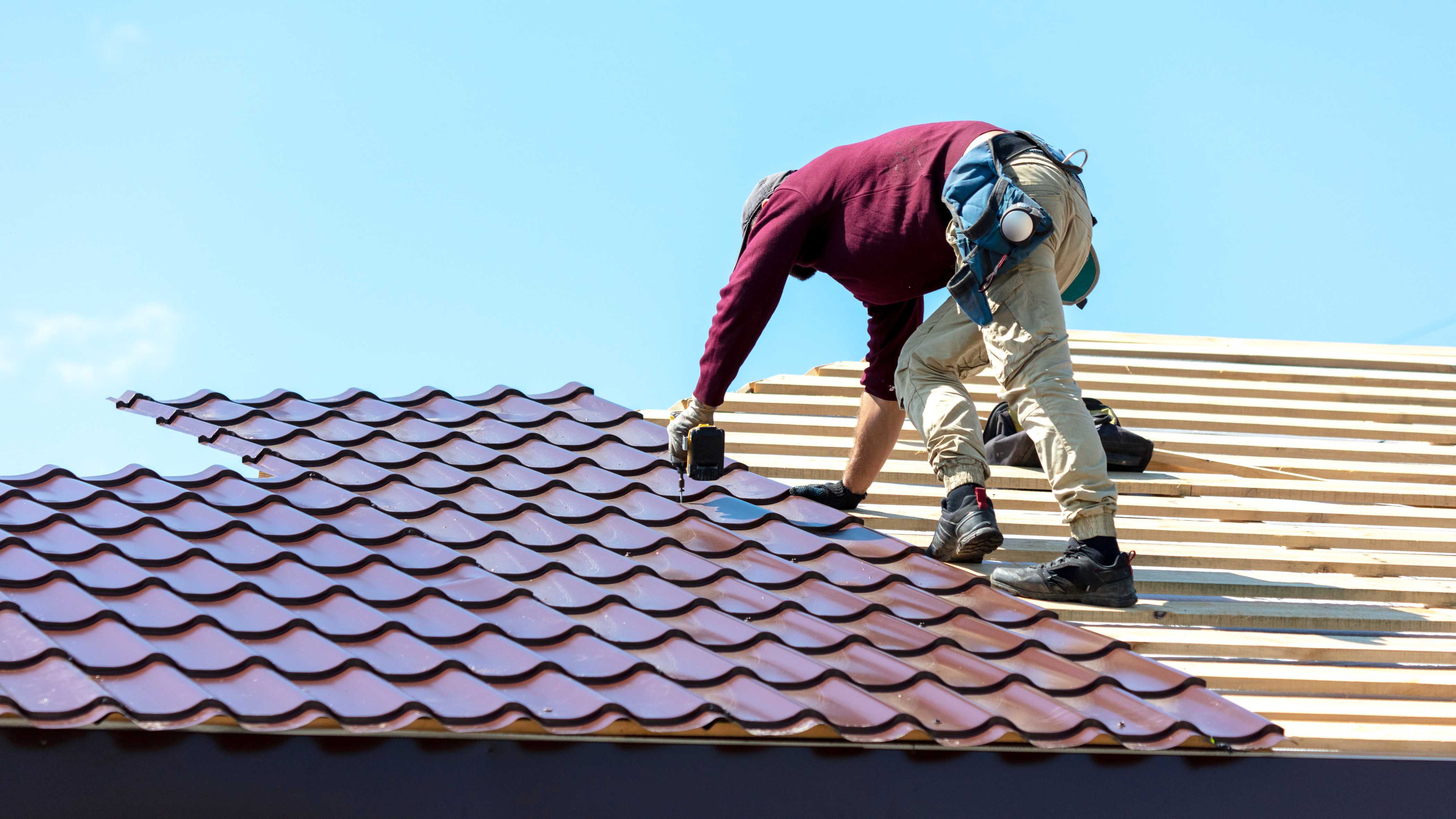 Contractor installing red metal tiles on the roof of a house